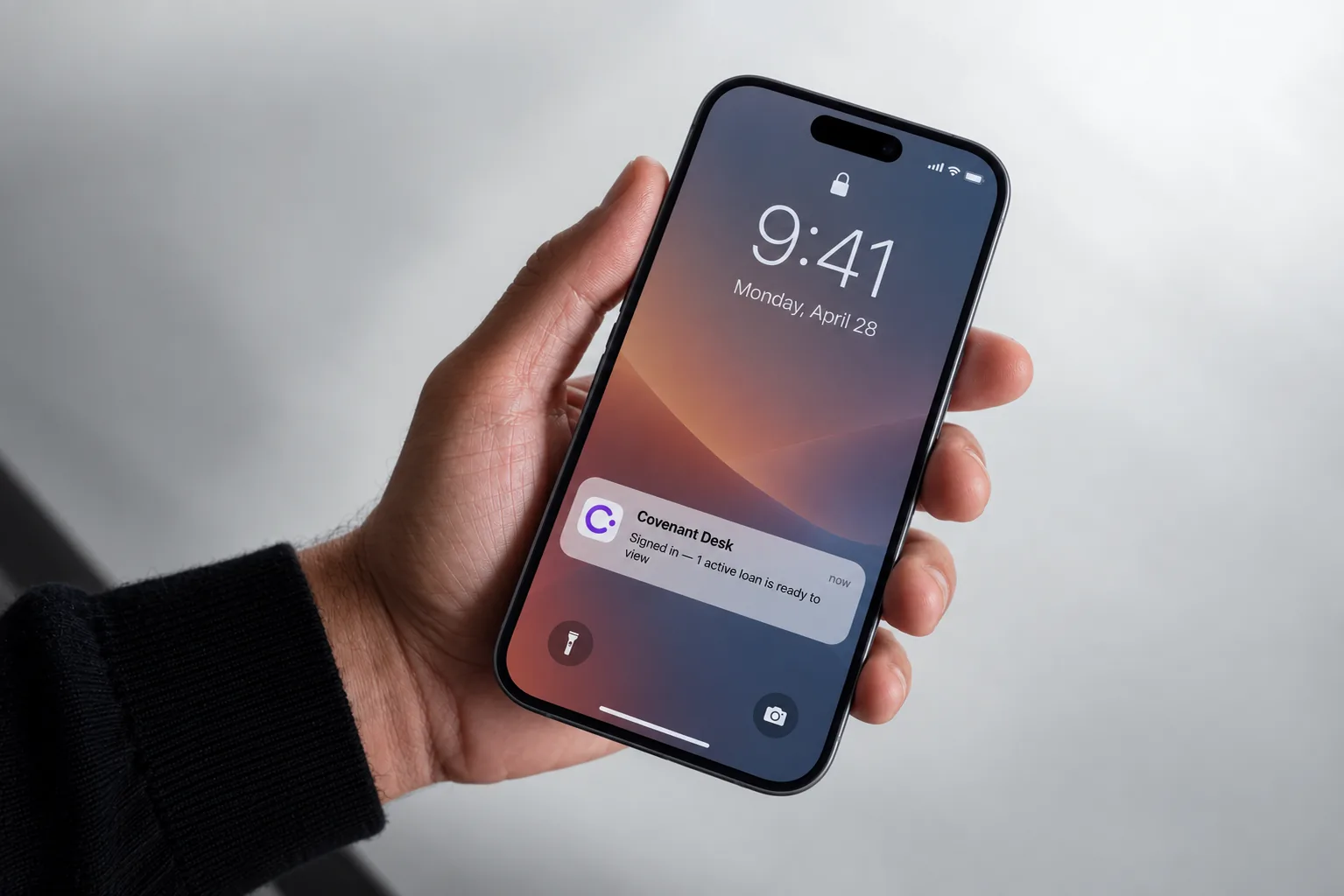 Hand holding a phone showing a Covenant Desk lock-screen notification: Signed in — 1 active loan is ready to view