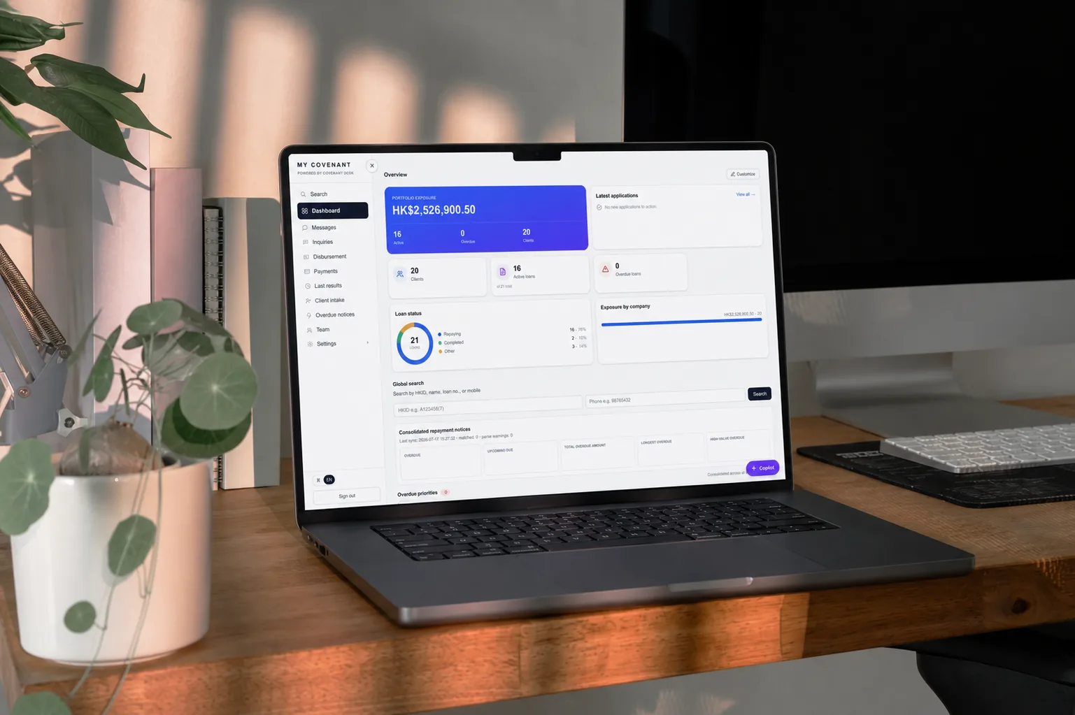 Laptop on a desk showing the Covenant Desk portal dashboard with loan status and portfolio exposure